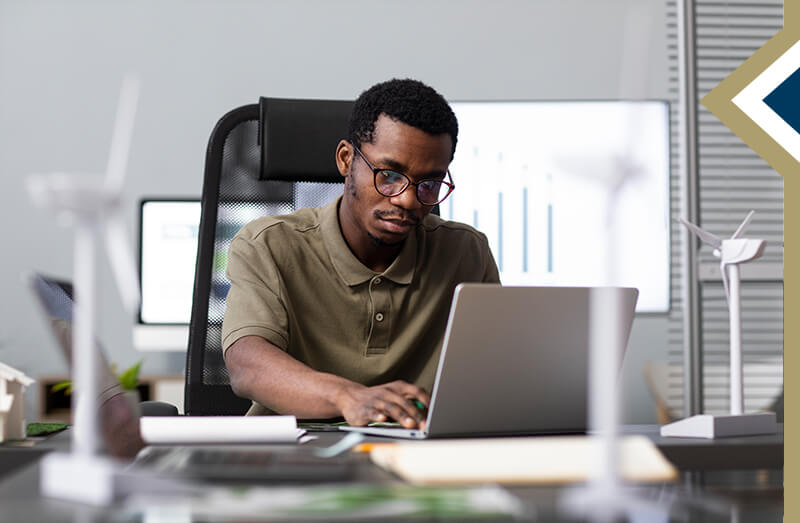 male working on laptop at desk with models of windmills sitting in front of him - photo credit: Freepik
