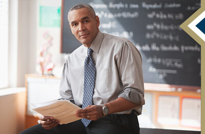 professional male sits on desk in front of chalkboard
