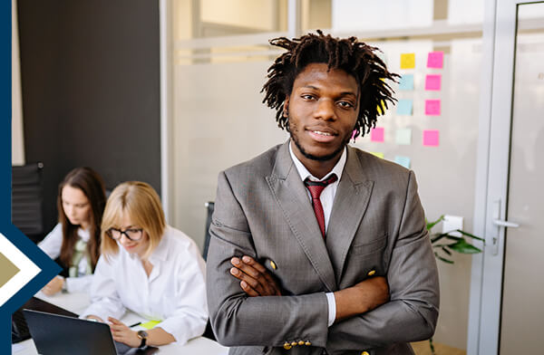 professional male looks directly at the camera, colleagues and wall with post-it notes in the background behind him