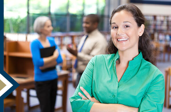 professional female smiles at camera in library, colleagues talk in background