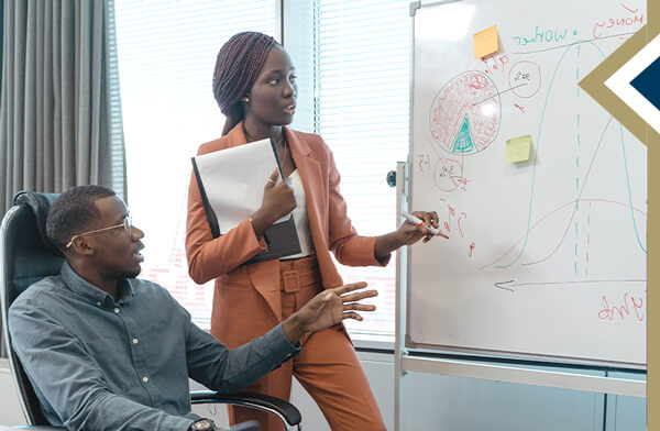 professional female leads discussion of data written on a white board with male colleague seated next to her