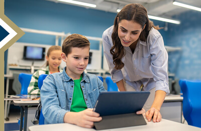 teacher leans forward to assist middle school student on tablet (Image credit: Freepik)