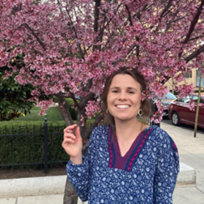 Mara Moettus smiles for photo in front of cherry tree, holds cherry blossom in her fingers