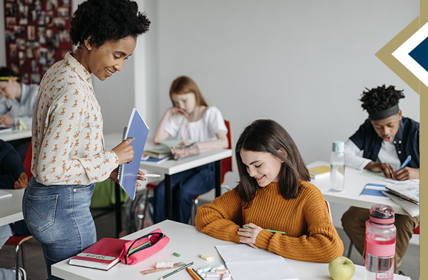 Teacher smiles and looks down to review work on middle school student's desk while walking by