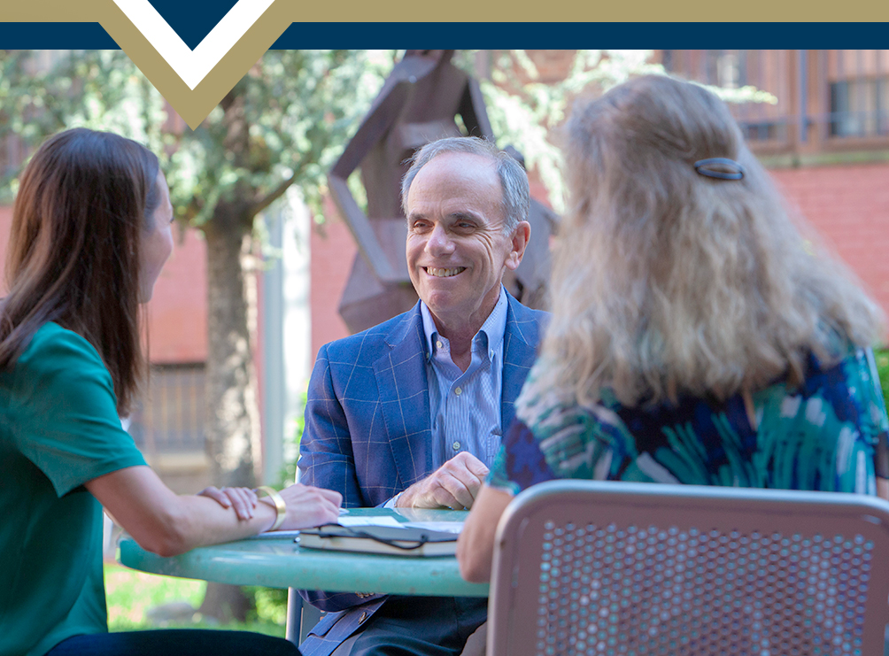 Dr. Feuer speaks to two GSEHD students at outdoor table
