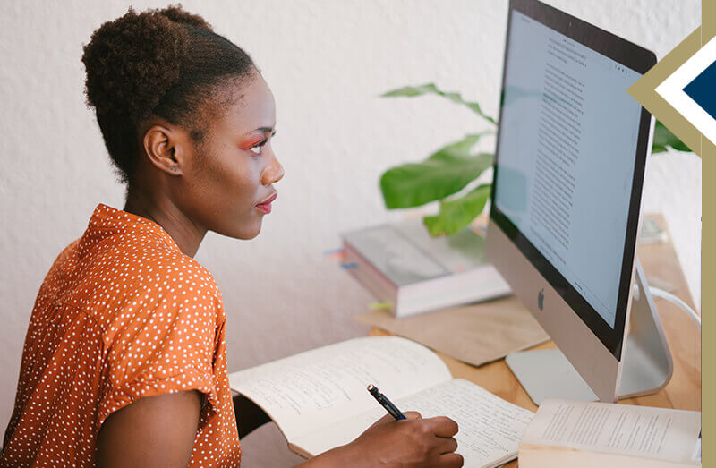 professional female takes notes in notebook while looking at computer screen