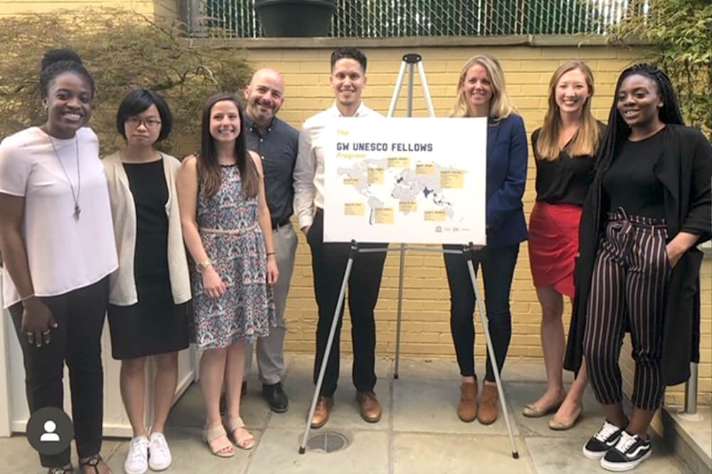 2018 GW UNESCO Fellows pose for group photo around easel with UNESCO fellowship sign