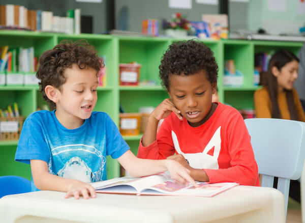 two divers kindergarten students share a book in the school library