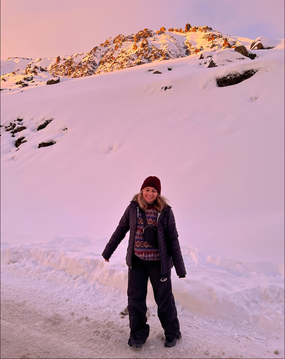 Stacey poses in front of the snowy landscape along the side of the road; pink overlay as the sun sets