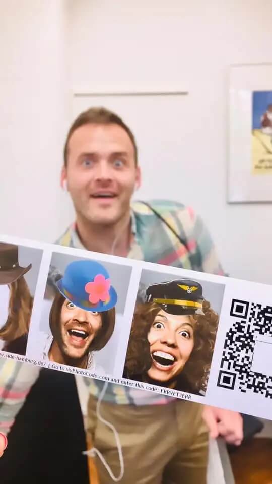 Kyle Hall holding print out of silly photos of people wearing hats