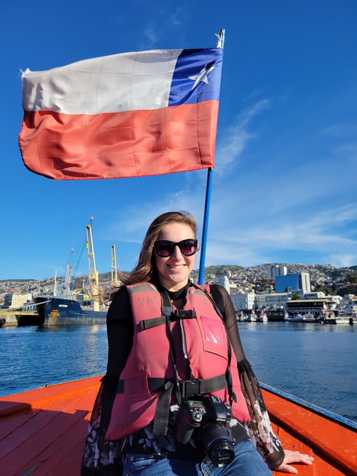 Caroline smiles for a photo on a boat in Puerto Valparaíso with flag waving above her