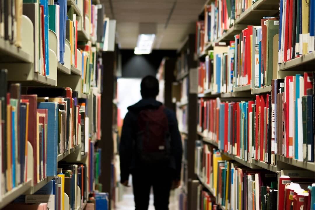student walks through the aisle of library shelves filled with books