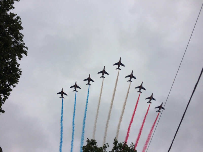 9 planes fly overhead in a V shape, three releasing blue smoke, three in the middle releasing white smoke, and three on the right releasing red smoke to represent the country's colors