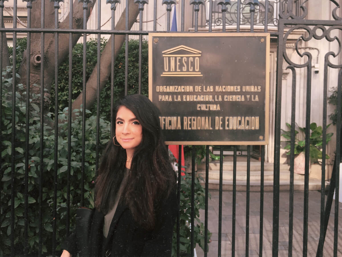 Renny poses for a photo in front of the UNESCO sign hanging on a gate in front of the building
