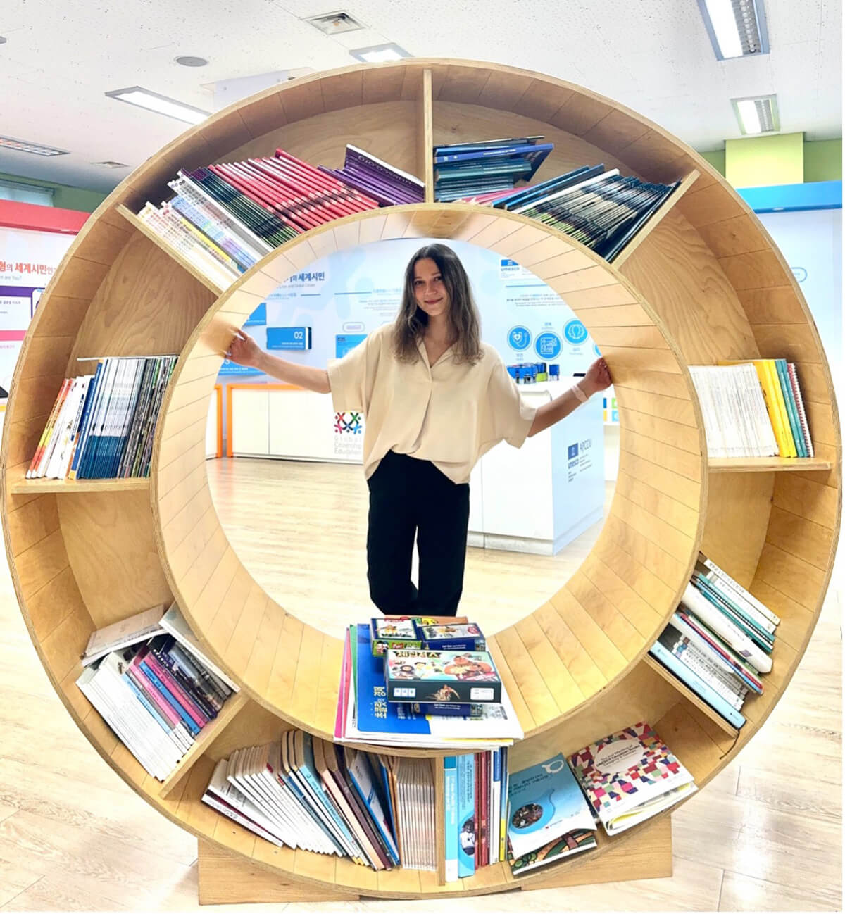 Kseniia poses behind a large round bookshelf, designed to represent the UN Sustainable Development Goals logo