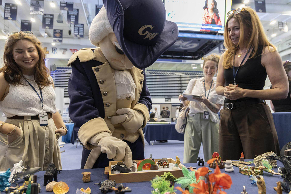 George (mascot) tries out the sand tray at a booth manned by play therapy specialists, including graduate student Haley Giles (left) and Clinical Assistant Professor of Counseling and Human Development Mary DeRaedt (right). 