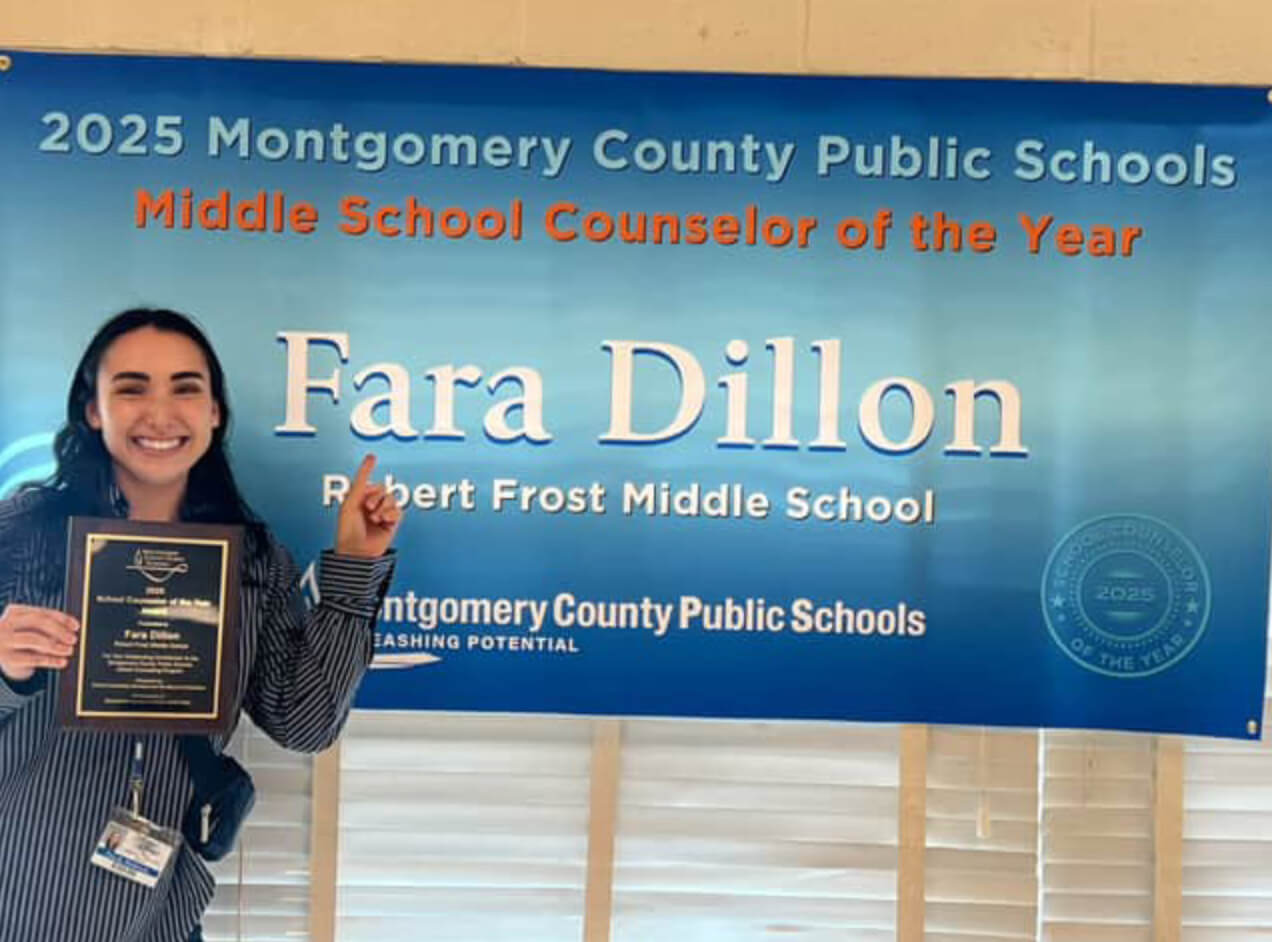 Fara Dillon holds award while pointing to "2025 Montgomery County Public Schools Middle School Counselor of the Year" banner