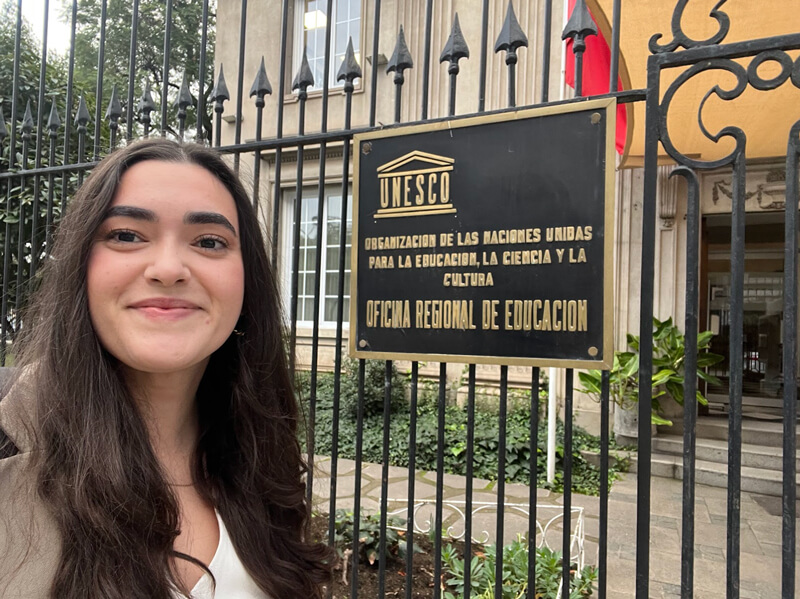 Mia takes a selfie in front of the gate to the UNESCO Santiago office