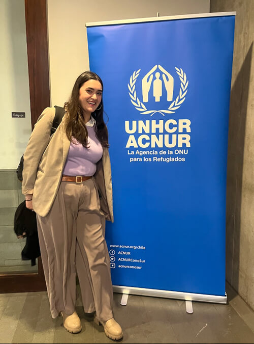 Mia poses for photo in front of event banner at World Refugee Day Storytelling event