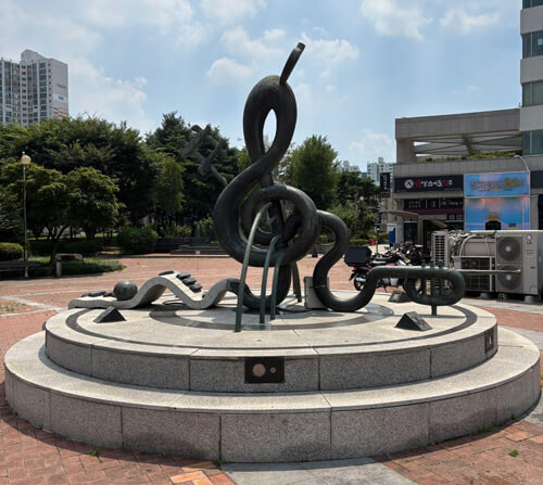 A metal art structure outside of a building resembling a treble clef