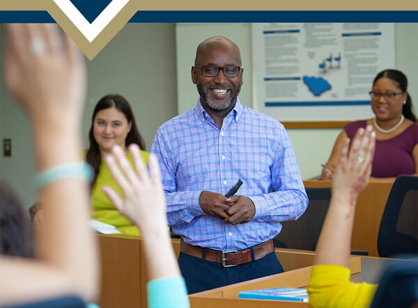 Dr. Howard stands in the center of a classroom, students in the foreground raise their hands