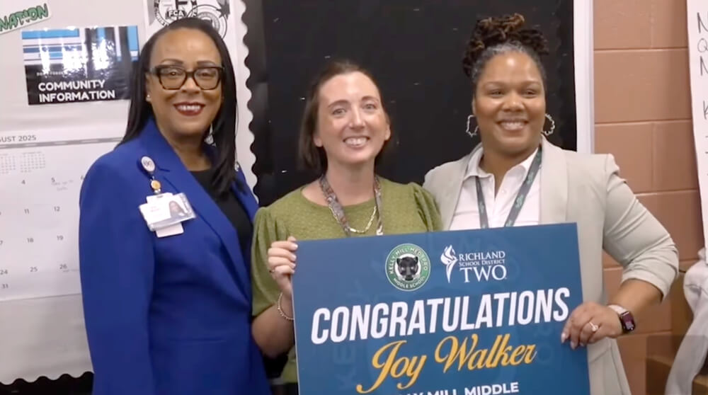 Joy Walker, posing with her superintendent Dr. Moore and another school leader, is presented with a sign that says "Congratulations, Joy Walker"