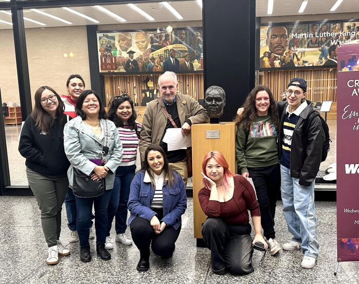 PhD students and Dr. Eakle pose for a group photo with a bust of MLK, Jr. at the MLK Library