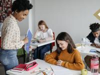 Teacher smiles and looks down to review work on middle school student's desk while walking by