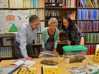 Dr. Carol O'Donnell, Douglas M. Lapp and Anne B. Keiser stand in a classroom, leaning over some desks with clear animal crates on them."