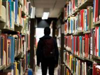 student walks through the aisle of library shelves filled with books