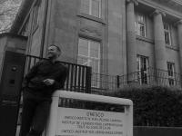 black and white photo of Kyle Hall posing by UNESCO UILL sign in front of the building
