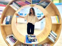 Kseniia poses behind a large round bookshelf, designed to represent the UN Sustainable Development Goals logo