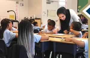 GSEHD alumna leans over desk to assist a student in her elementary classroom