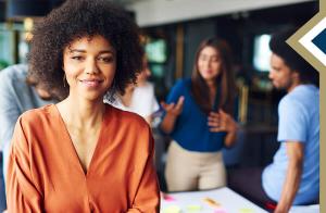young professional female smiles at camera, while group of other professionals talk behind her - photo credit: gpointstudio on Freepik