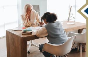 principal sits behind desk, student writes on paper on desk