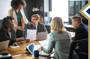 group of professionals around a conference table, one stands and presents paper to a colleague - photo credit: rawpixel.com on Freepik