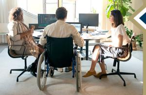 male in a wheelchair and two females sit at a conference table