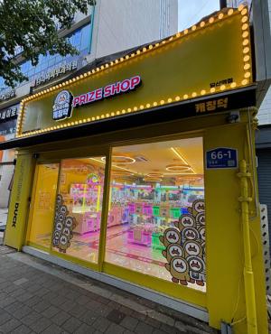 yellow store with sign that reads “Prize Shop;” Inside, you can see bright lights and games where patrons can play games and select prizes