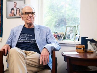 Dean Feuer sits in office chair; Photo Credit: Arwen Clemans, Senior Photo Editor, The Hatchet