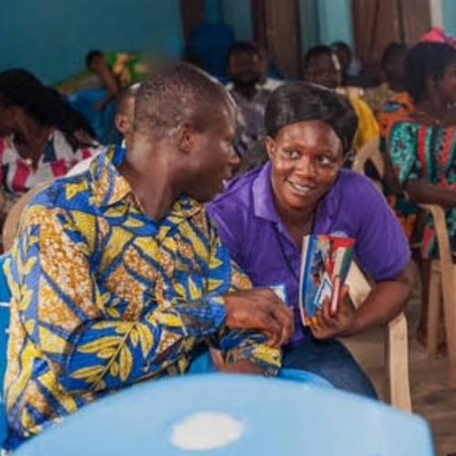 two guests at the IIES event lean in to speak to each other, other seated guests in the audience surround them 