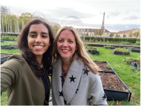 Maha Malik and Dr. Laura Engel pose for a photo in a garden with the Eiffel Tower in the distance