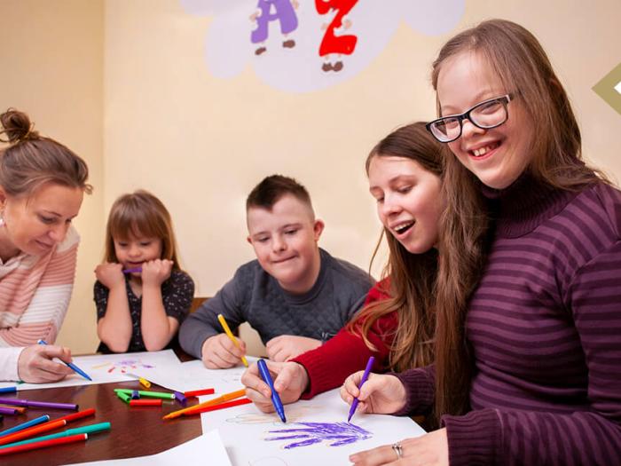 image of special education teacher helping students with an art project; one student smiles at the camera