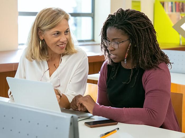 professional female assists young adult on computer in library