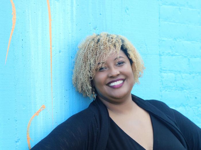 Deniece Dortch smiles for photo in front of bright blue brick wall (contributed photo)