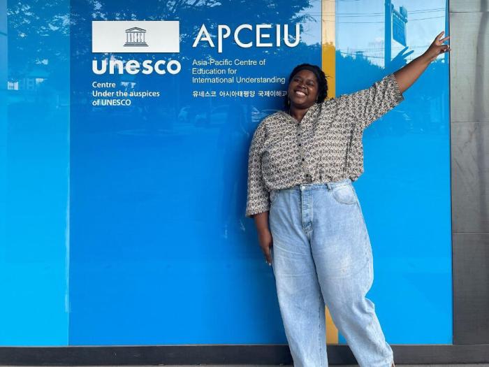 Micha standing and making a peace sign in front of APCEIU logo 