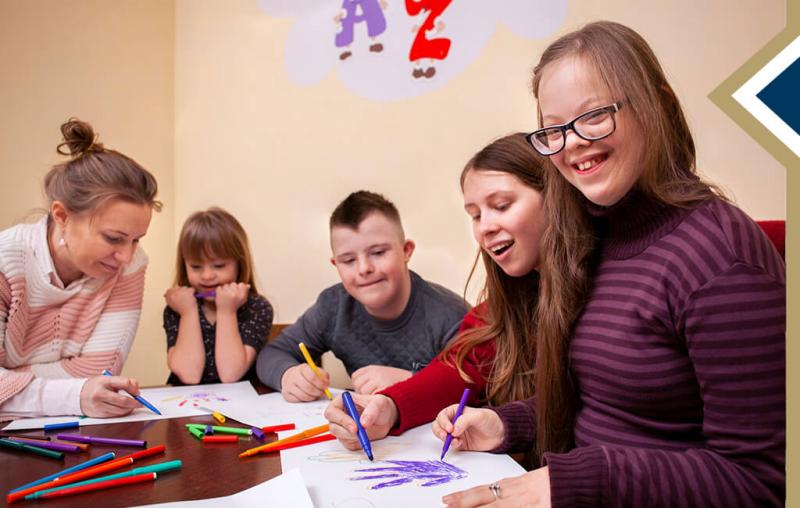 image of special education teacher helping students with an art project; one student smiles at the camera