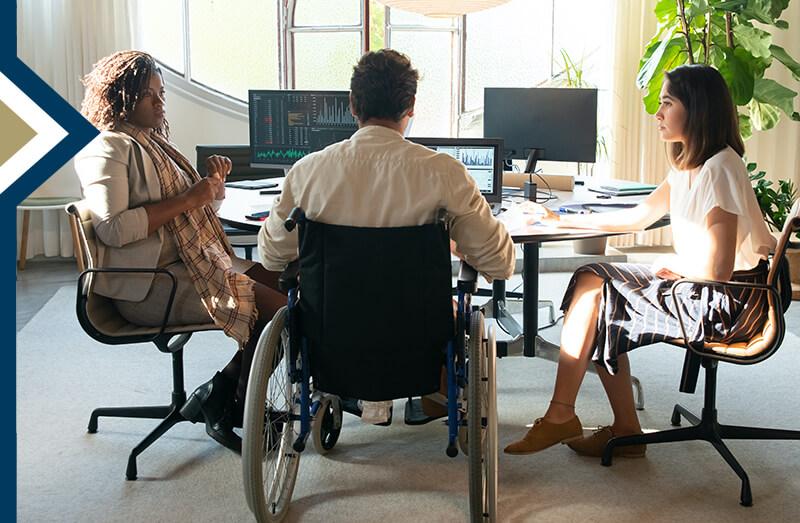 professional male in wheelchair reviews data with two colleagues seated next to him at table