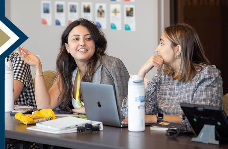 Two GSEHD students sitting at desk in Israel Education class, one talks while other looks at her