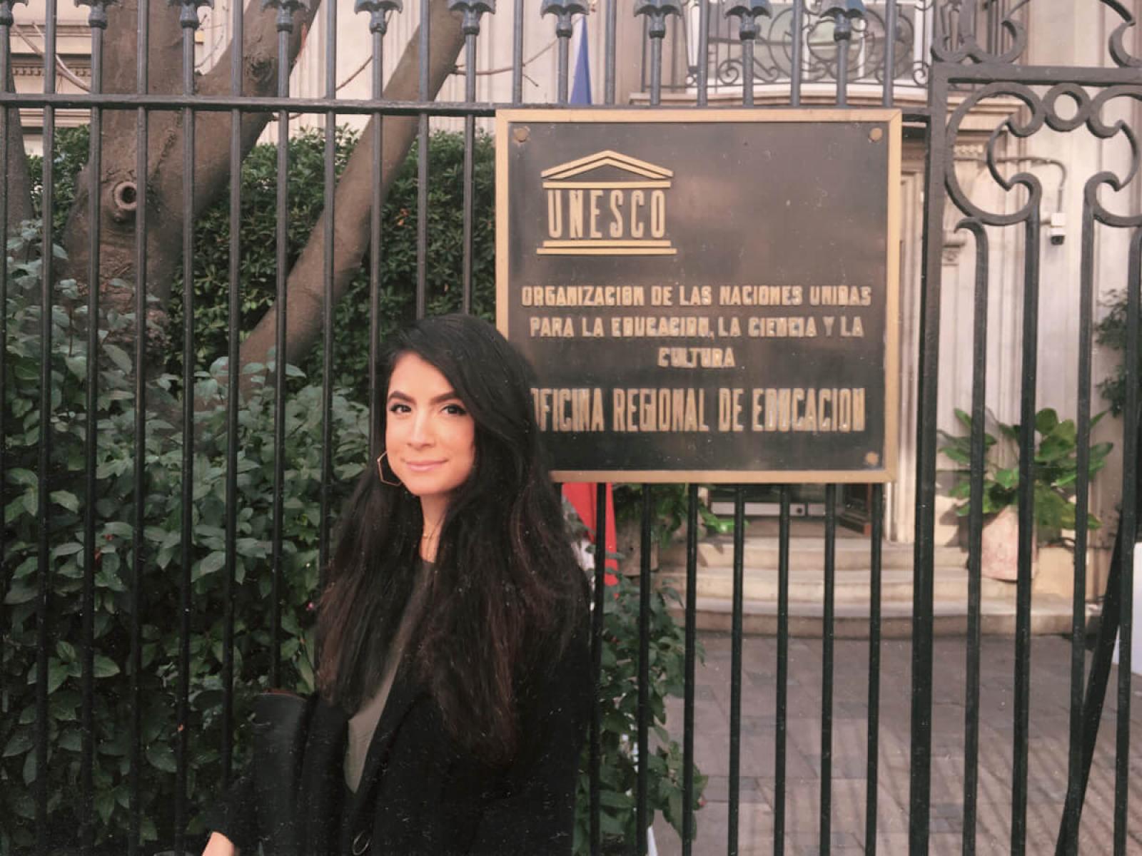 Renny poses for a photo in front of the UNESCO sign hanging on a gate in front of the building