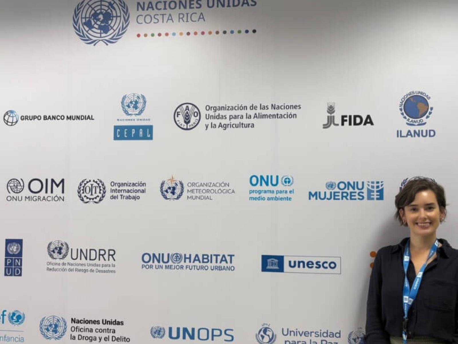 Lily poses for a photo in front of a step-and-repeat banner with various logos At the UNESCO office in San Jose Costa Rica